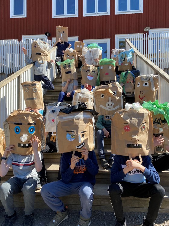 Elever sitter i trappa med masker gjorda av papperspåsar på huvudet
