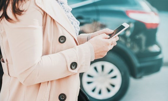 Kvinna med mobil vid sidan om parkerad bil. Foto: Shutterstock