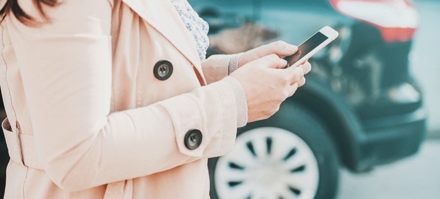 Kvinna med mobil vid sidan om parkerad bil. Foto: Shutterstock